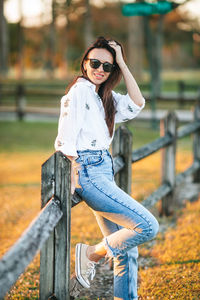 Portrait of young woman standing against fence