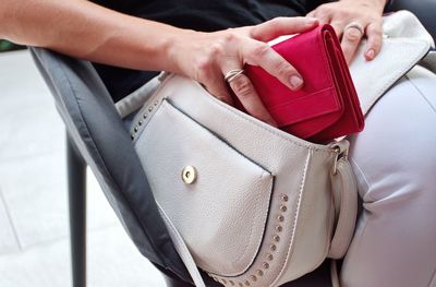 Midsection of woman holding purse while sitting on chair