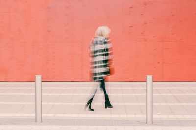 Woman walking on footpath against wall