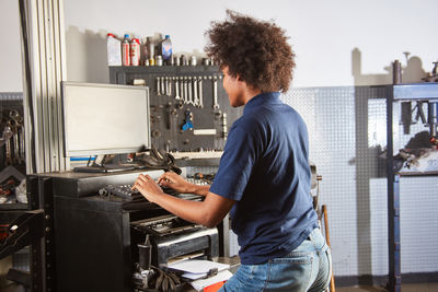 Rear view of mechanic using computer at garage
