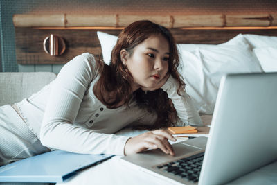 Young woman using laptop while lying on sofa at home