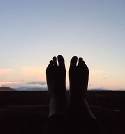 Low section of silhouette woman resting against clear sky during sunset