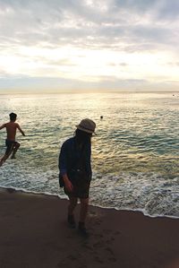 Rear view of woman standing on beach against cloudy sky