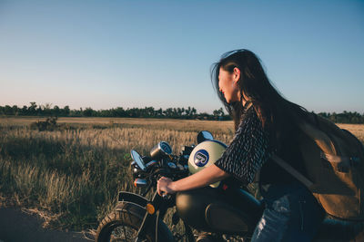 Woman riding motorcycle on field against clear sky