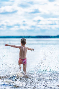 Full length of shirtless boy in sea against sky