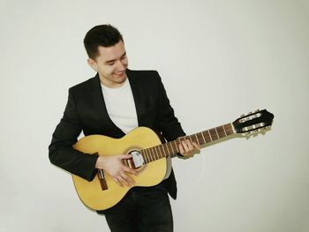 Smiling man playing guitar while standing against white background