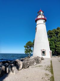 Lighthouse by sea against clear sky