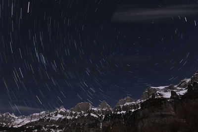 Low angle view of mountains against star trails at night