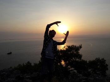 Silhouette person standing by sea against sky during sunset