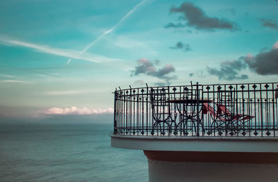 Metal railing by sea against sky