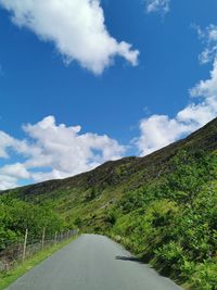 Road amidst green landscape against blue sky