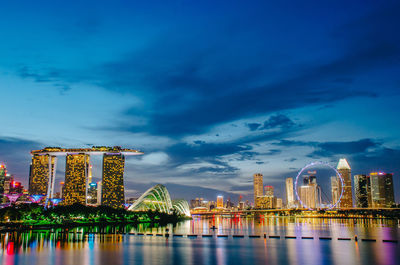 Illuminated city by river against sky at night