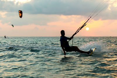 Man surfing in sea against sky during sunset