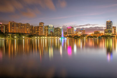 Scenic view of lake by illuminated cityscape at dusk