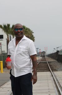 Portrait of man holding cocktail shaker while standing on railroad track