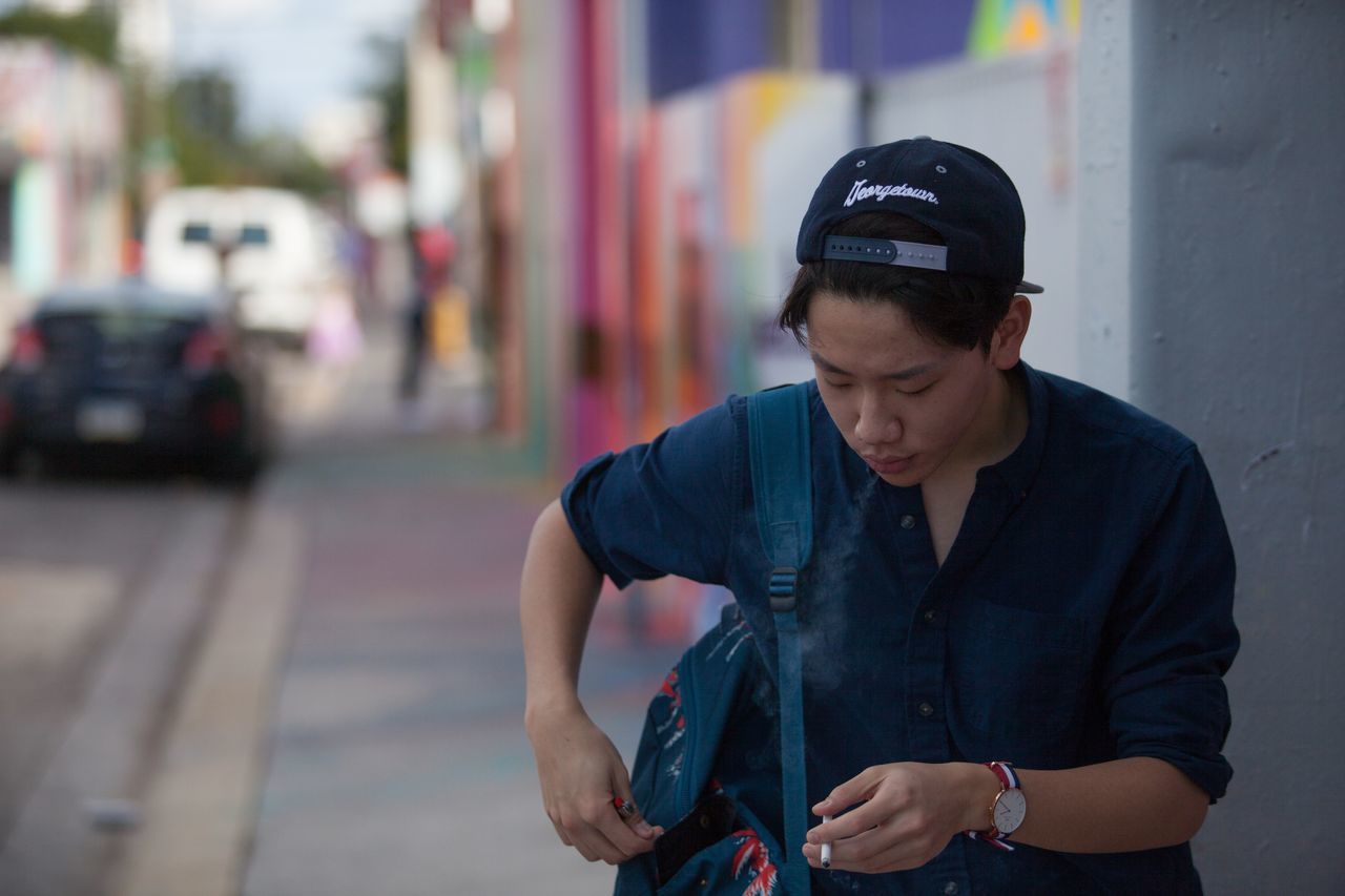 YOUNG MAN USING PHONE WHILE STANDING ON CITY