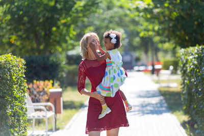 Woman holding happy daughter on footpath in park