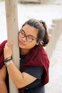 Young thoughtful woman holding on wooden post at beach