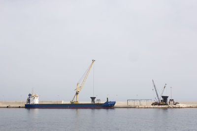 Ship by crane at harbor against sky