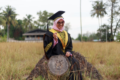 Portrait of woman in graduation gown sitting on log