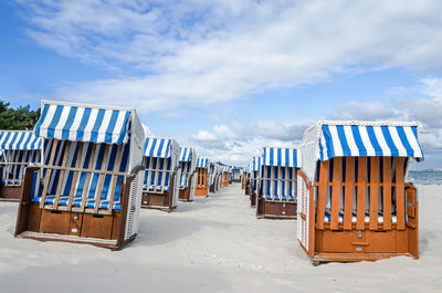 Hooded chairs on beach against sky