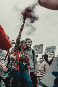 Young woman with arms raised against sky in city