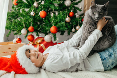 Portrait of a happy teenage girl and her gray maine coon cat next to a decorated christmas tree. 