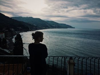 Rear view of woman looking at sea against cloudy sky