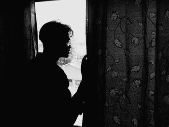 Silhouette of man looking through window at home