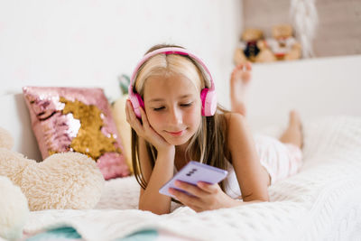 Attractive caucasian girl holds a smartphone and looks at it while lying on the bed. a teenager