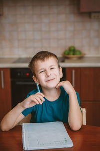 Cute child writing letters in notebook sitting by table in kitchen