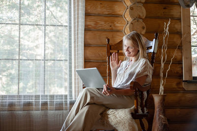 Smiling woman talking on video call while sitting on chair at home