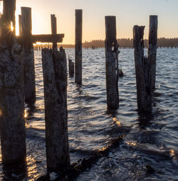 Wooden posts on sea against sky during sunset