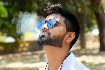 Close-up of man wearing sunglasses while smoking against trees