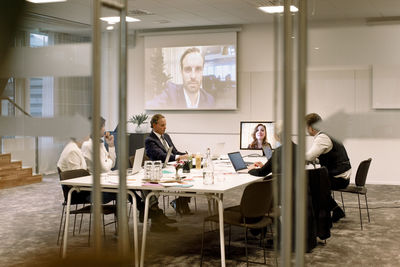 Business executives discussing in meeting during web conference seen through glass at office