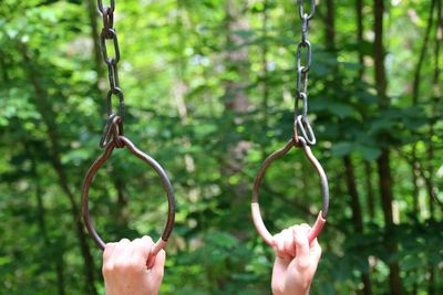 Cropped hands holding metallic handles hanging in forest