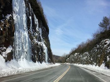Frozen waterfall on mountain by road against sky