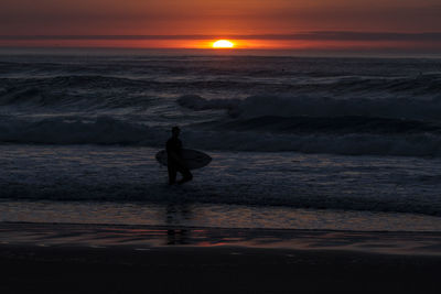 Silhouette man surfing on beach against sky during sunset