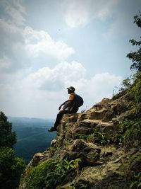 Man sitting on rock by mountain against sky