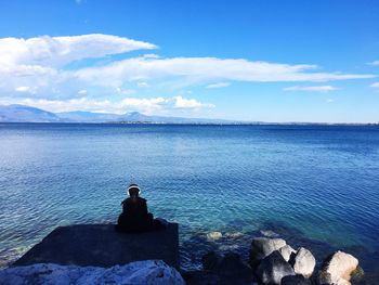 Rear view of woman sitting by sea against sky