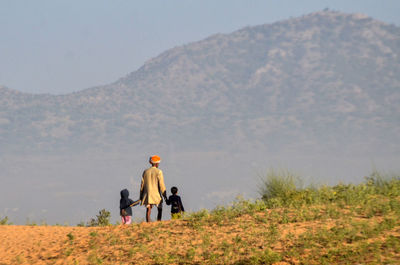Rear view of man with children walking on field against mountain