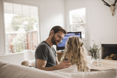 Father looking at daughter sitting on sofa in living room at home