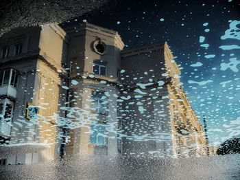 Wet street amidst buildings in city during winter