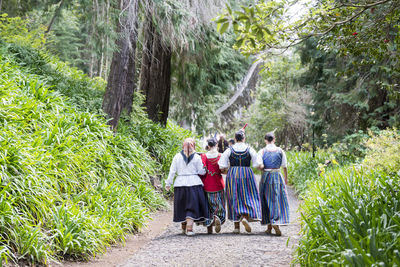 Rear view of people walking on road amidst trees