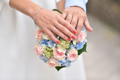 Hands of bride and groom with rings on wedding bouquet