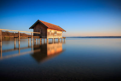 Stilt house in lake against clear sky during sunset