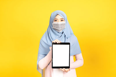 Portrait of person holding smart phone against yellow background