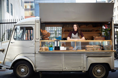 Portrait of smiling female owner standing in food truck parked on city street