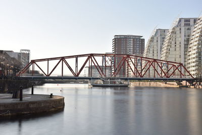 Bridge over river by buildings against sky in city