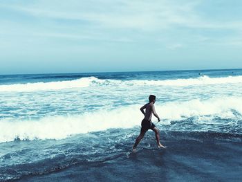 Shirtless man wading in sea against sky